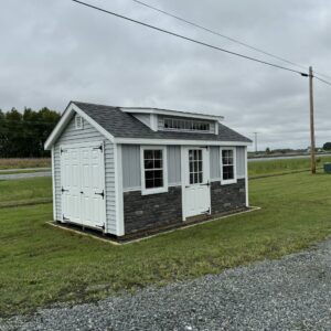 Gray and white storage shed with stone front pictured on lawn