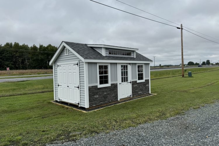 Gray and white storage shed with stone front pictured on lawn